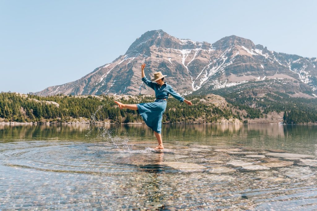 slow tourisme femme sur un lac qui joue avec l'eau derrière des montagnes voyage et environnement